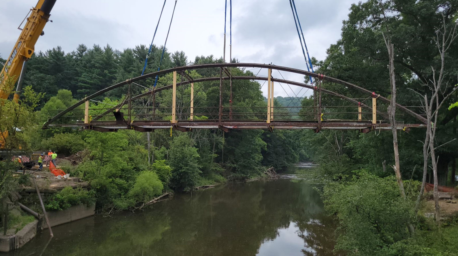 Straps lift up metal bridge over water.