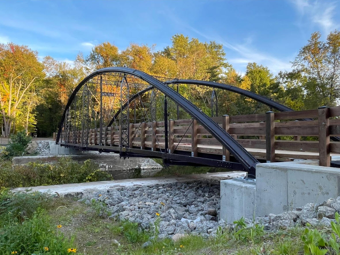Metal bridge with wood railings on concrete abutments over water.