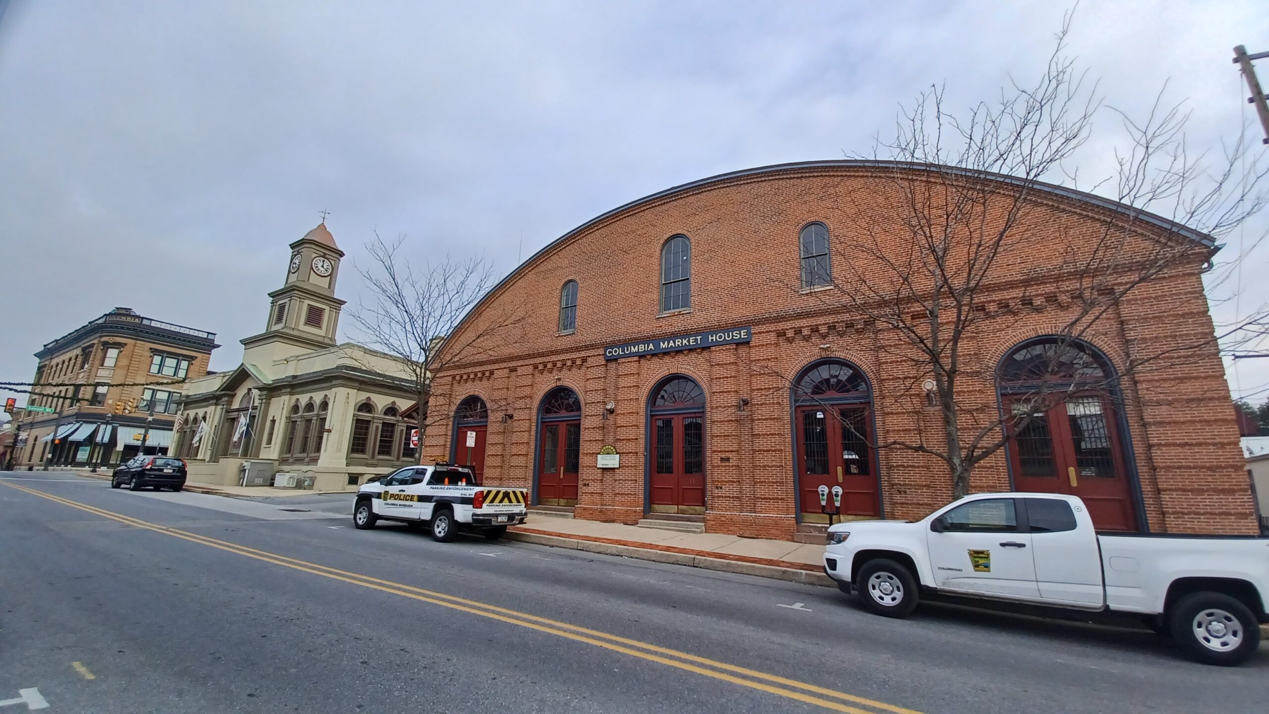 Streetscape in borough with large brick building with arched roof, building with a steeple, and three-story brick building.
