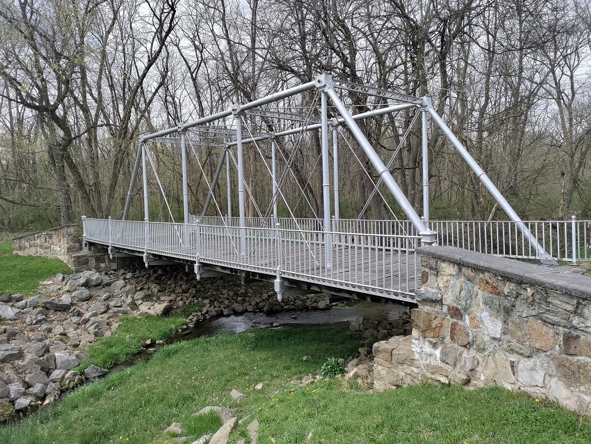 Metal bridge on stone walls over shallow creek.