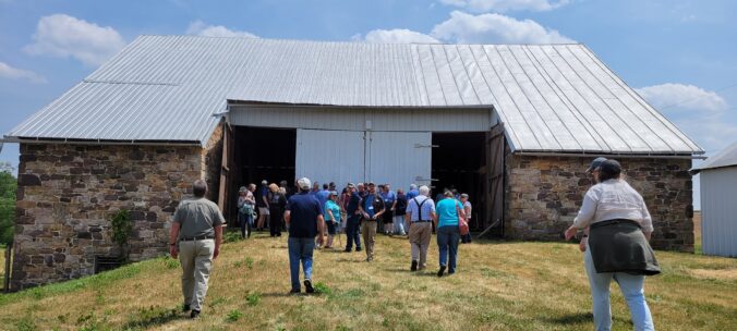 Large group of people standing in front of a bank barn.