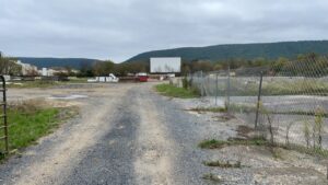 Gravel lot with buildings and large movie screen.