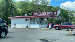 Small building surrounded by trees with large sign on roof that say Custer City Drive In