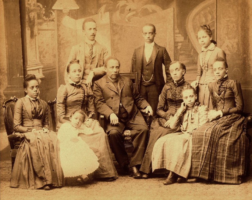 Black and white photograph of eight Black adults and two Black children sitting for a professional photographer.
