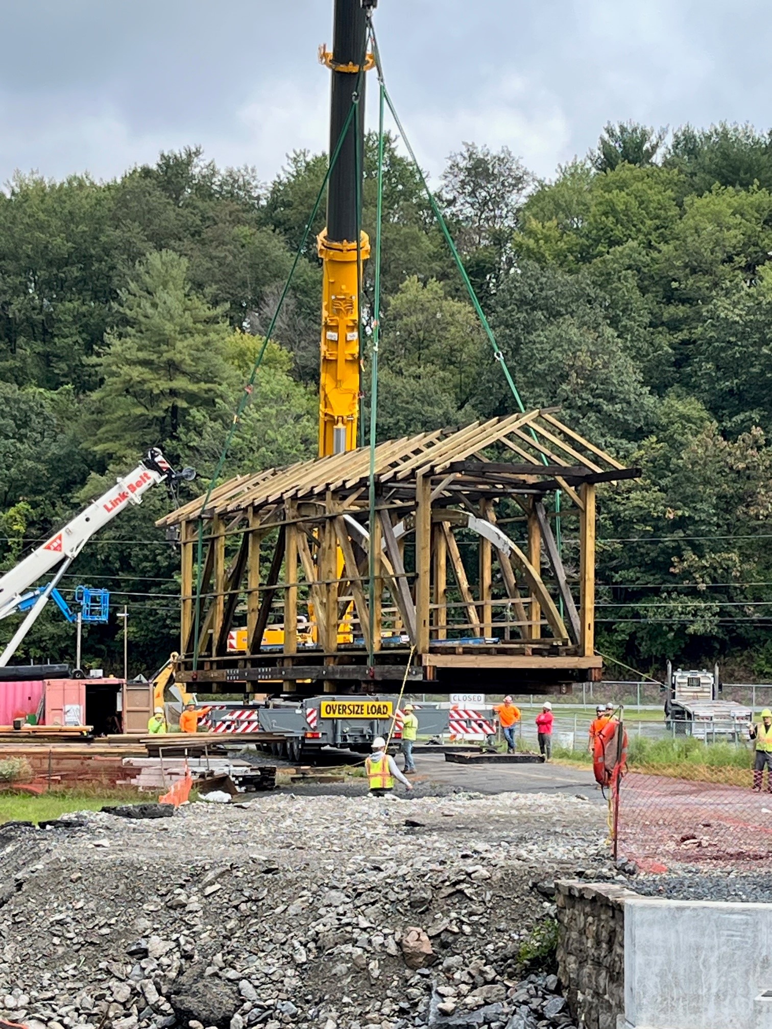 Large crane lifts wood skeleton of covered bridge off of the ground.