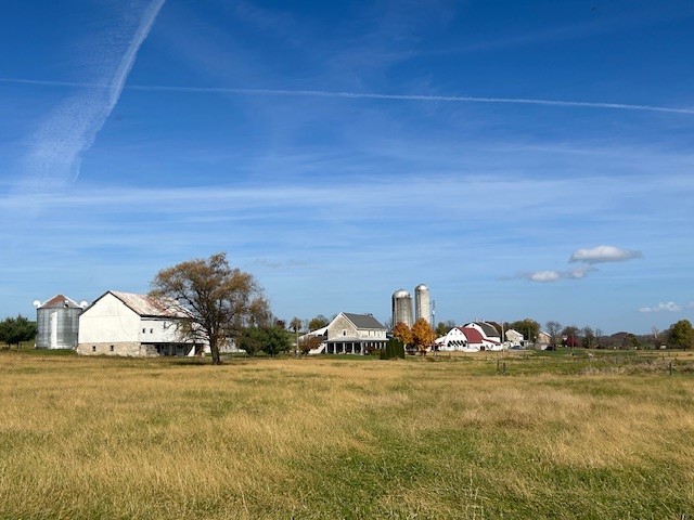 Standing in a field looking at a row of agricultural buildings like barns, houses, and silos.