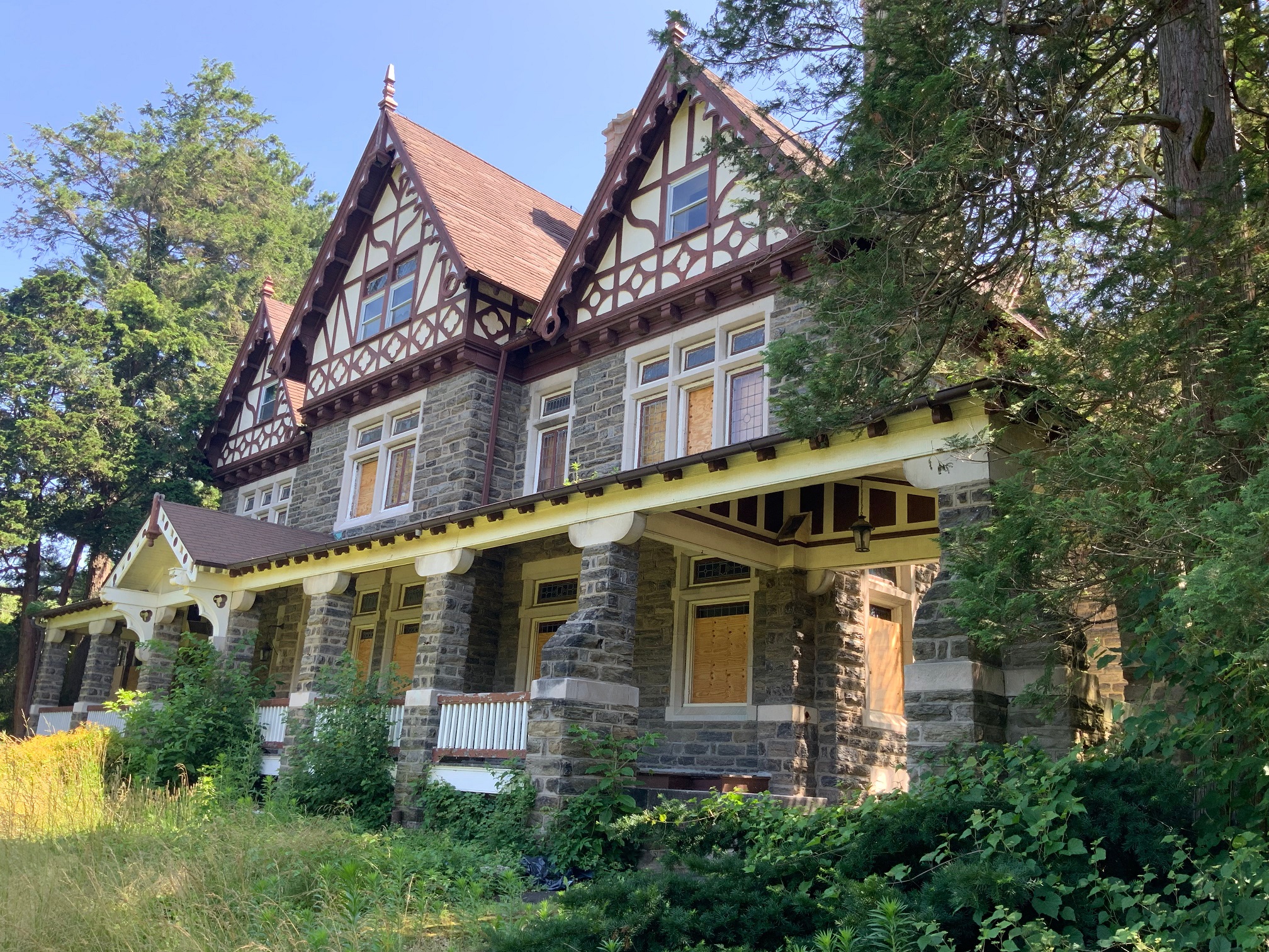 Three story stone and wood house with deep front porch, leaded glass windows, and three peaked roofs along the front.