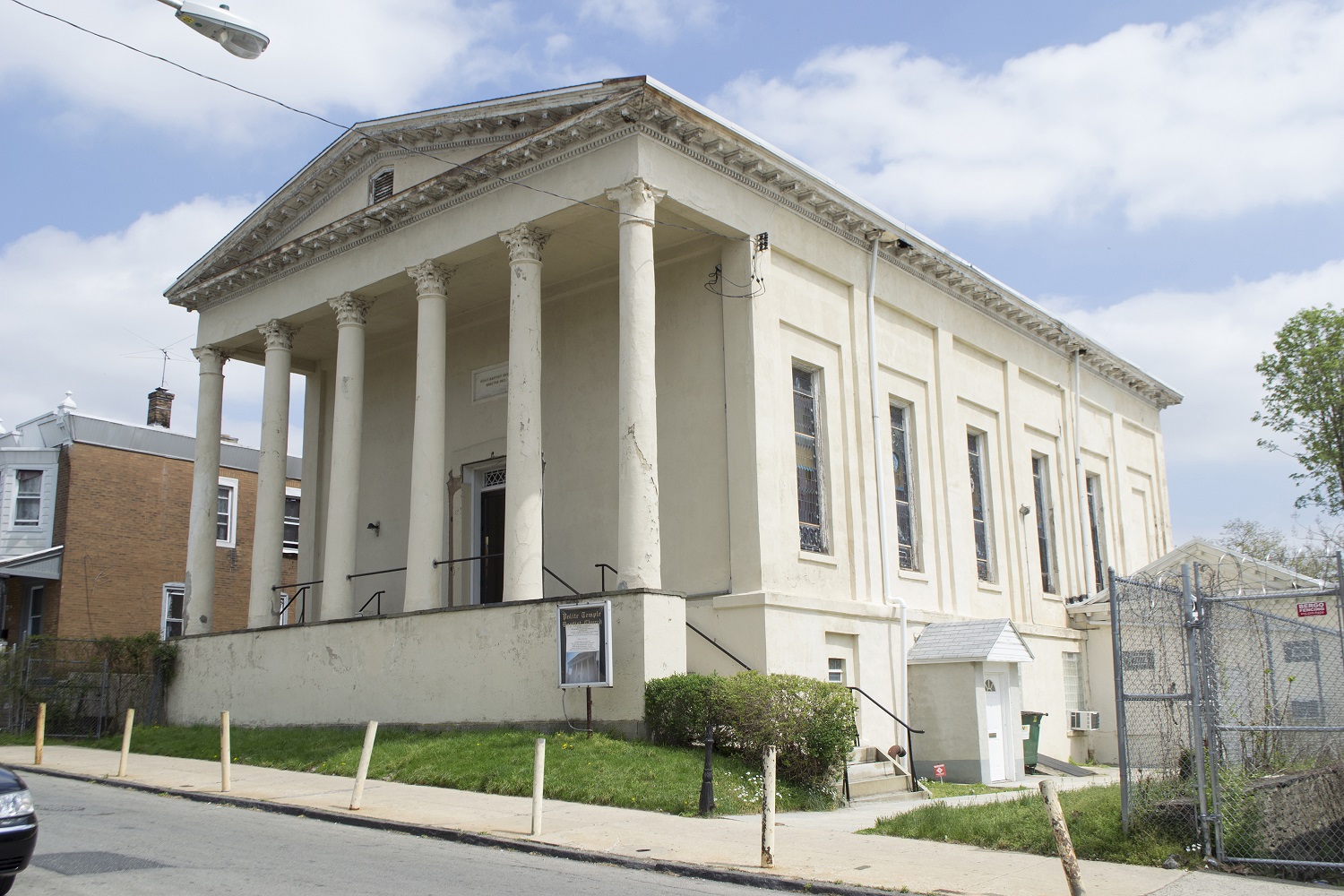 Large white building with six large, two-story columns along the street that support a triangular pediment. Stained glass windows line the side wall.