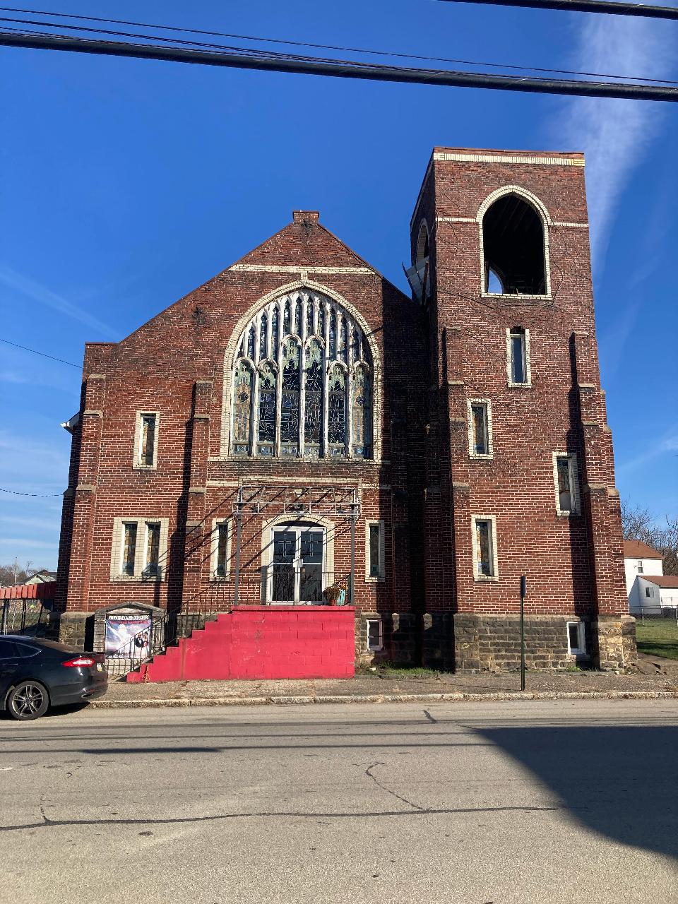 Brick Gothic Revival church with large stained glass window above entrance.