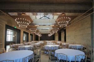 Large room with concrete walls, many round tables, and large chandeliers.