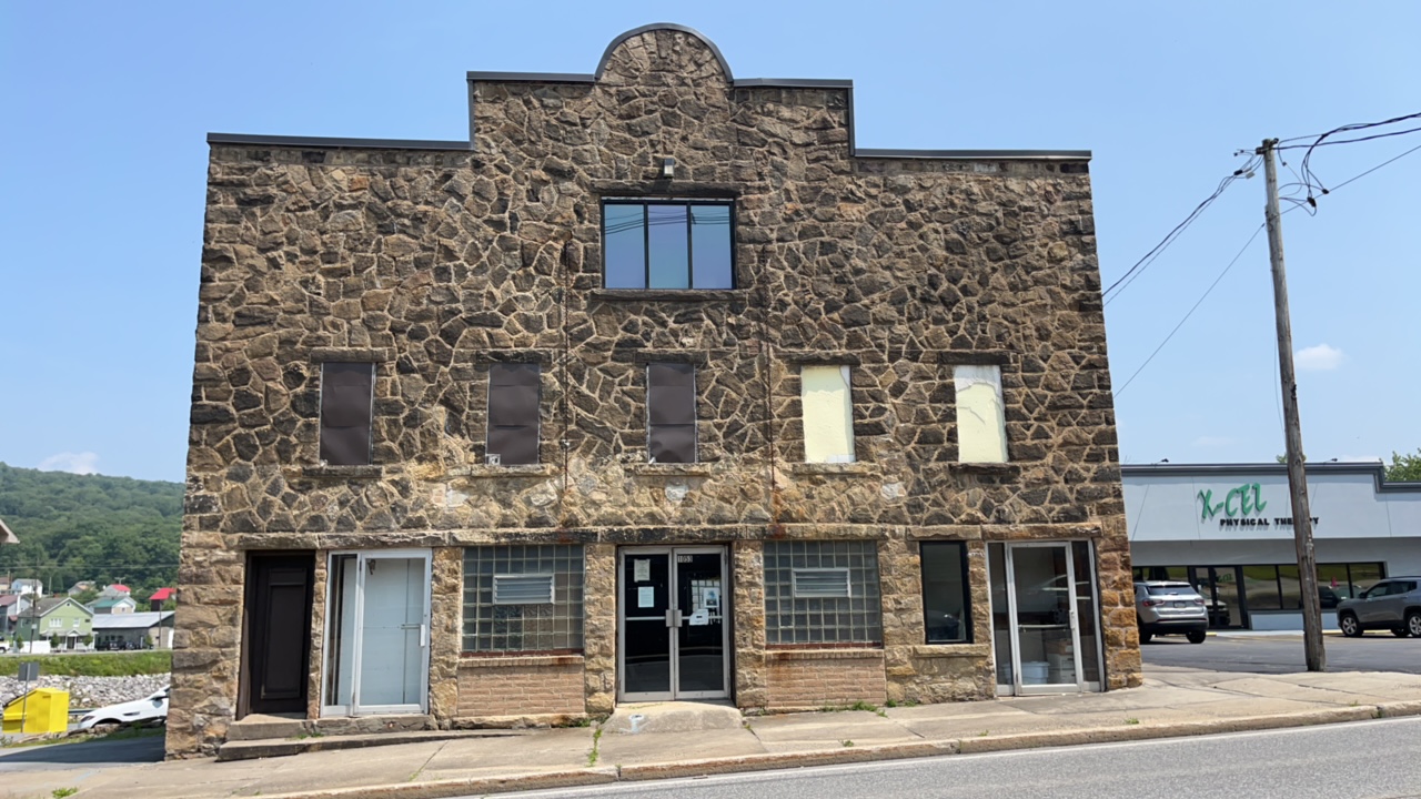 Three-story stone building with first floor storefronts along sidewalk.