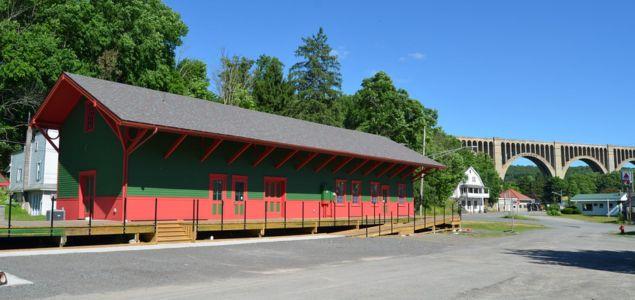 Long one-story wood building with steep roof next to a paved road.