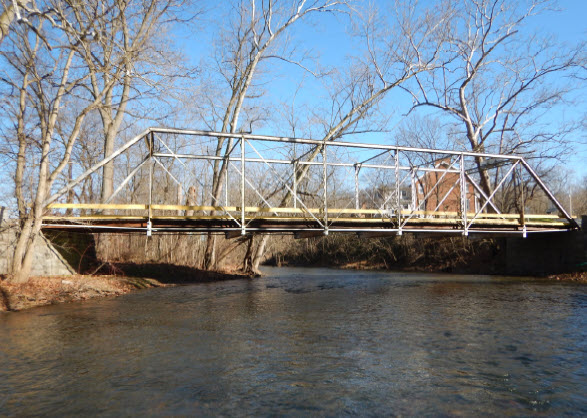 Simple metal truss bridge over wide shallow creek.