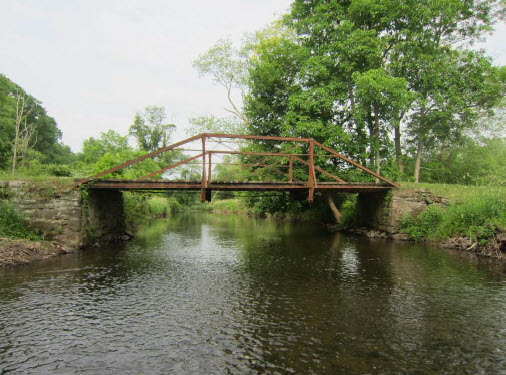 Metal truss bridge over water with wooded and grass areas at either end.