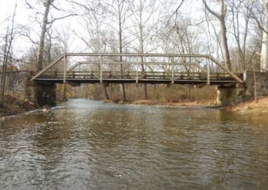 Metal truss bridge over wide creek.