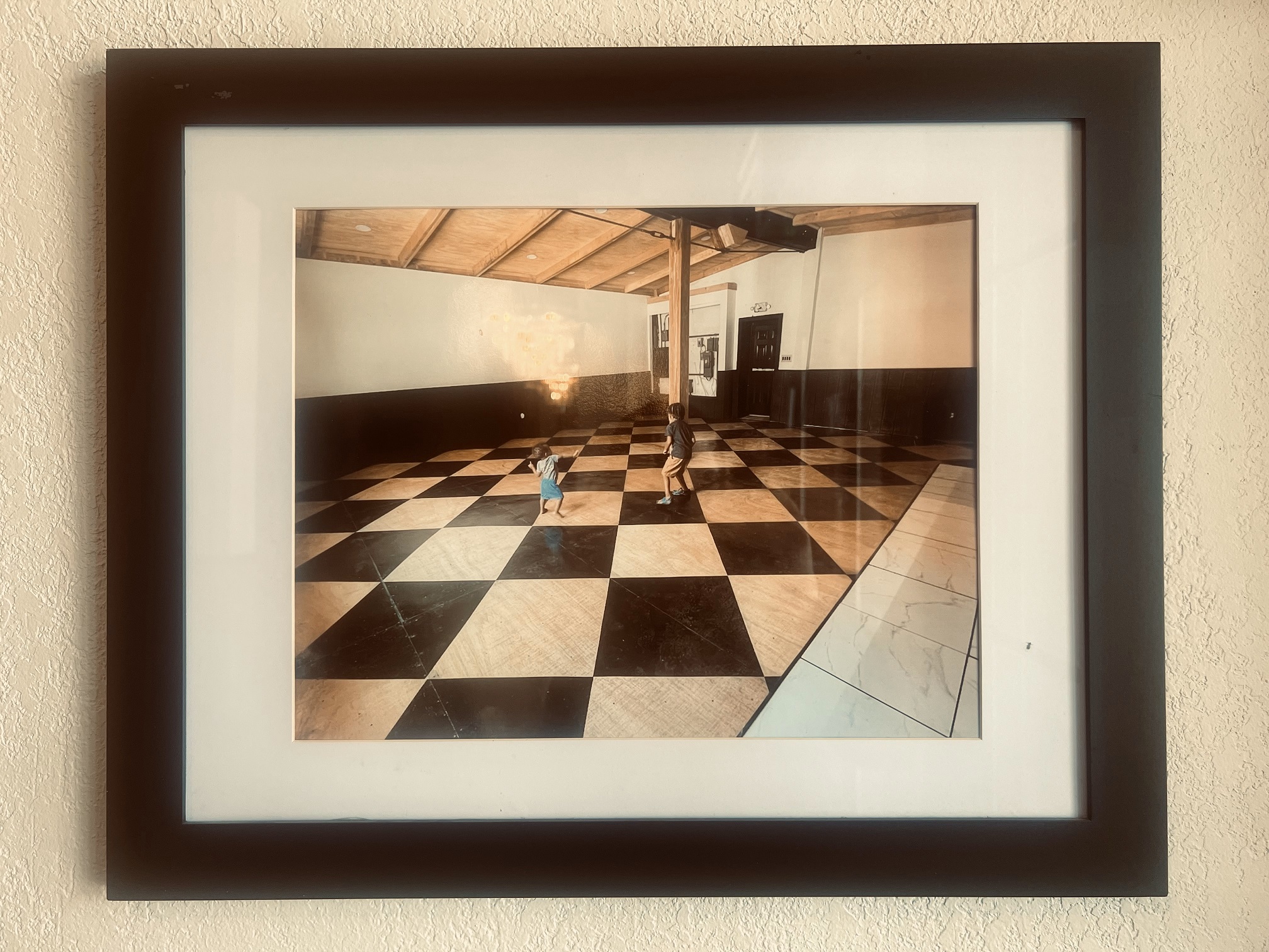 Framed photograph of two children playing on a black and white diamond pattern floor.