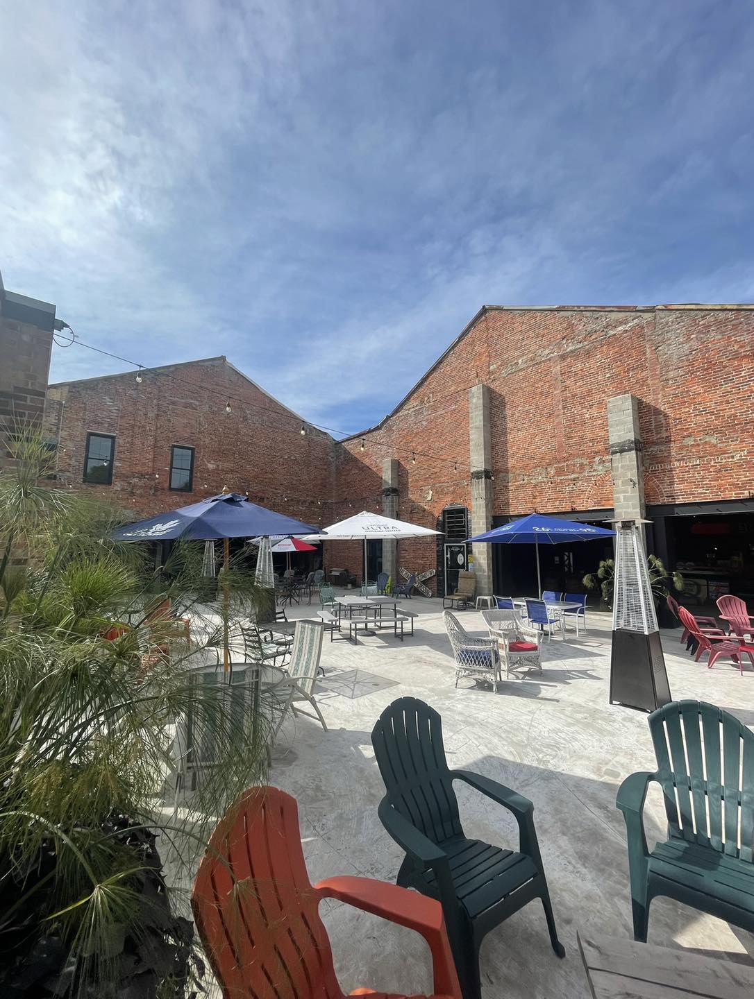 Concrete patio next to two large brick walls and filled with chairs and tables.