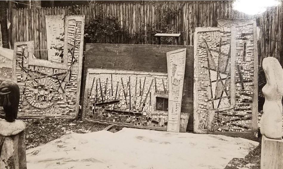 Three panels of tile murals propped against a wood fence.