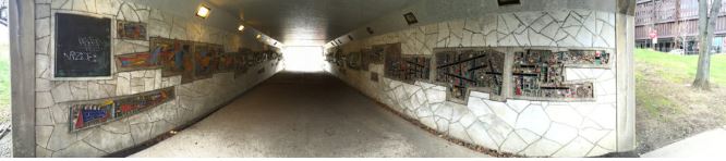 Looking through a pedestrian tunnel with decorative murals on two walls.