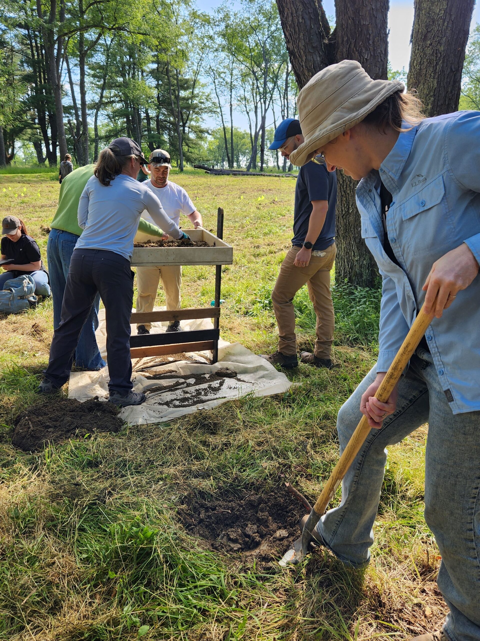 One person digs in the dirt while others screen it through a sifter.