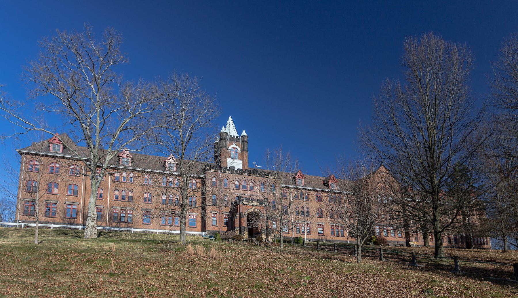 Very large 3-story brick building with center tower on a wooded hillside.