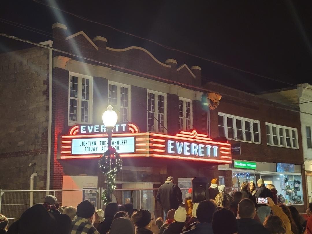 Large group of people in street at night in front of brick buildings.