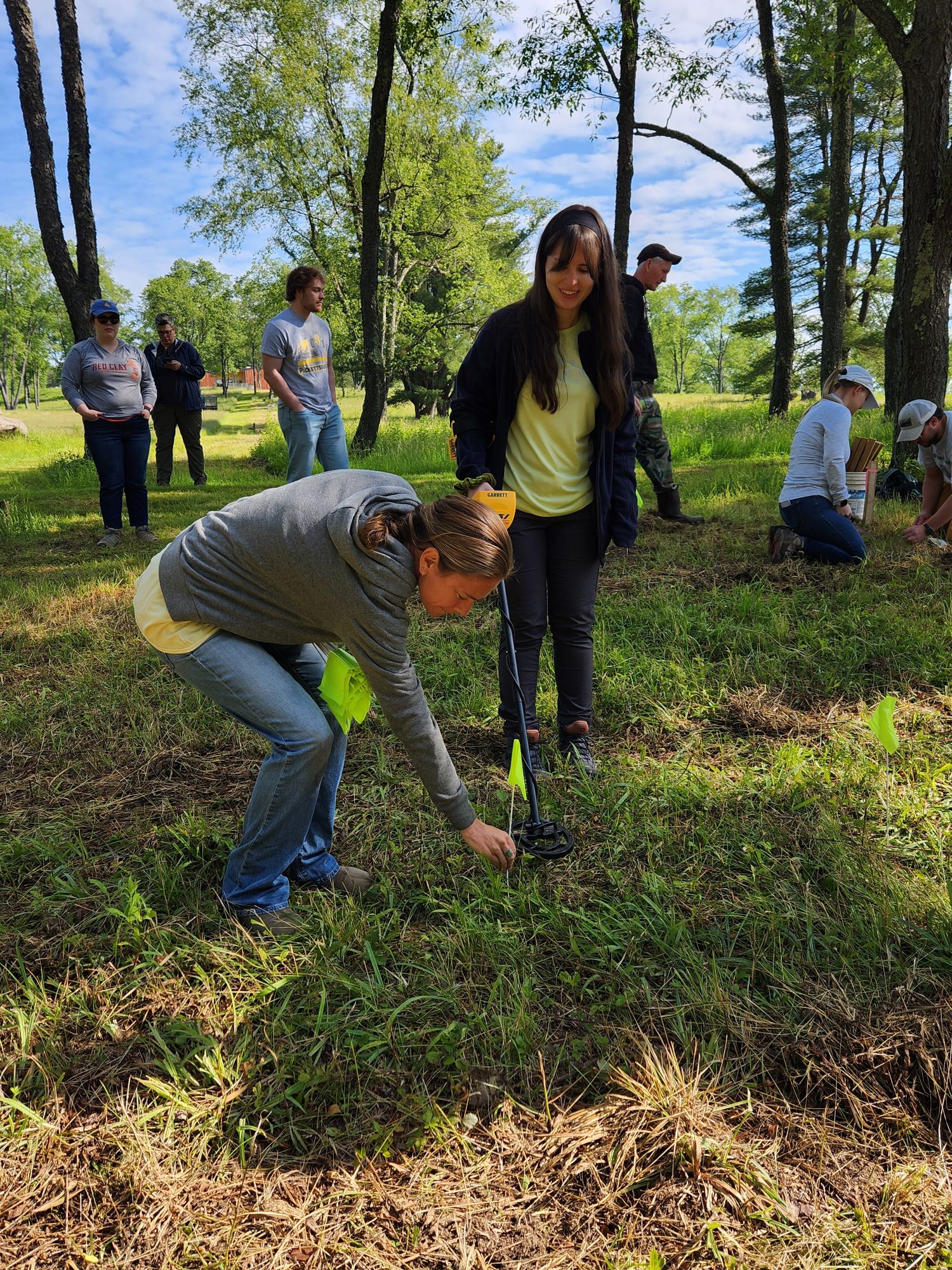 Woman uses long tool on grass while another woman places a flag.