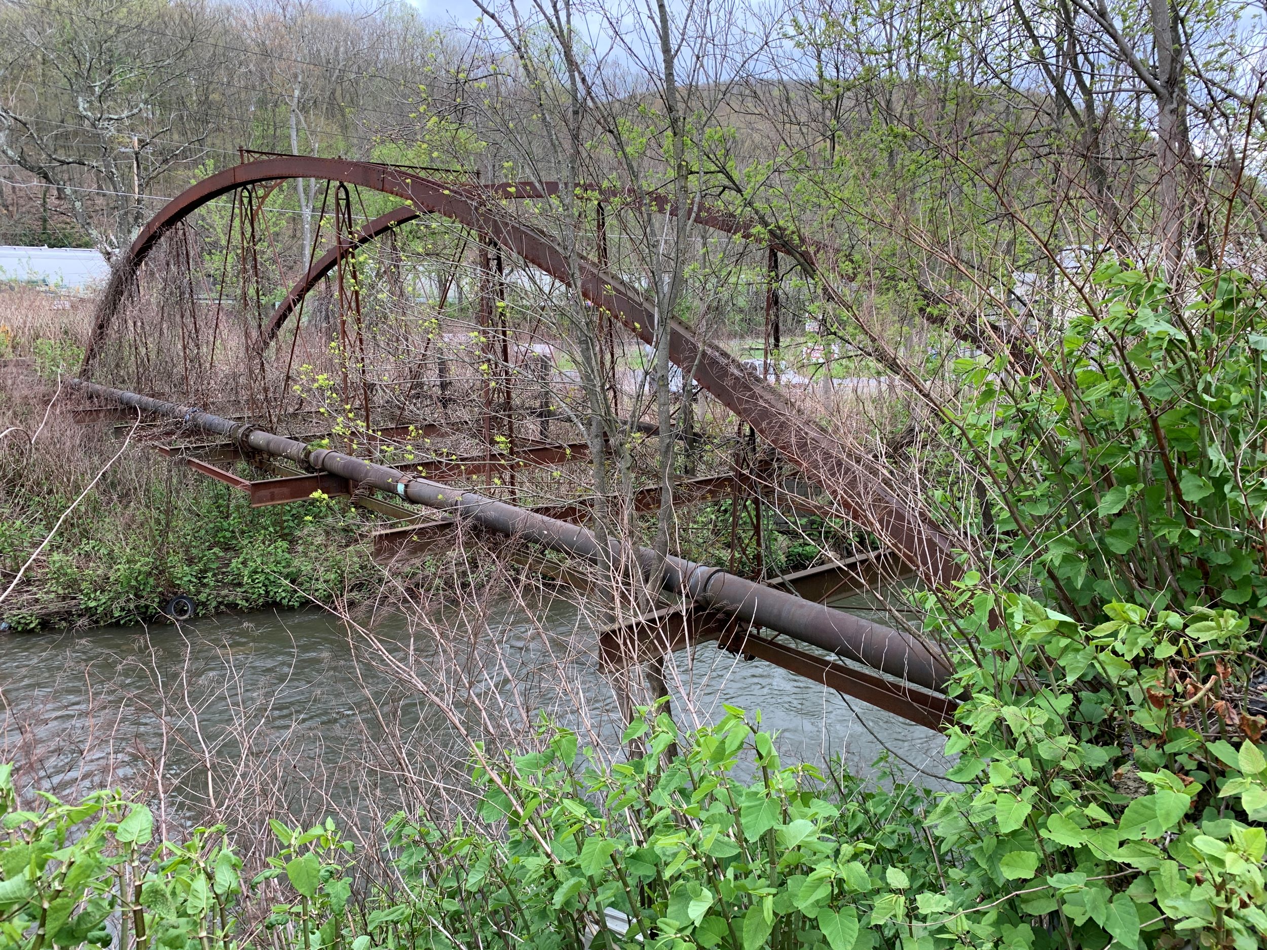 Metal truss bridge over water in a wooded area.