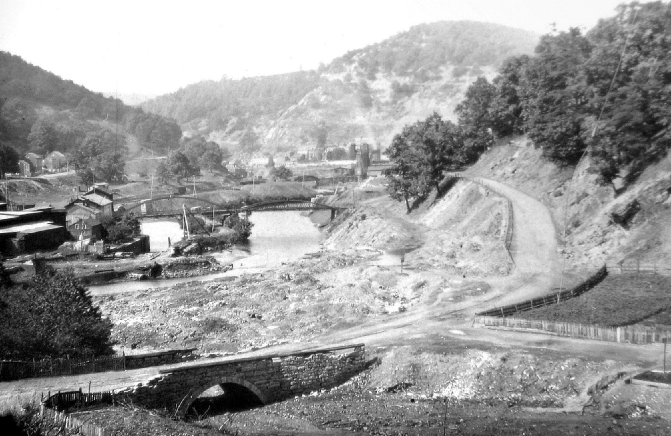 Black and white postcard showing two bridges over water in mountain and wooded area.