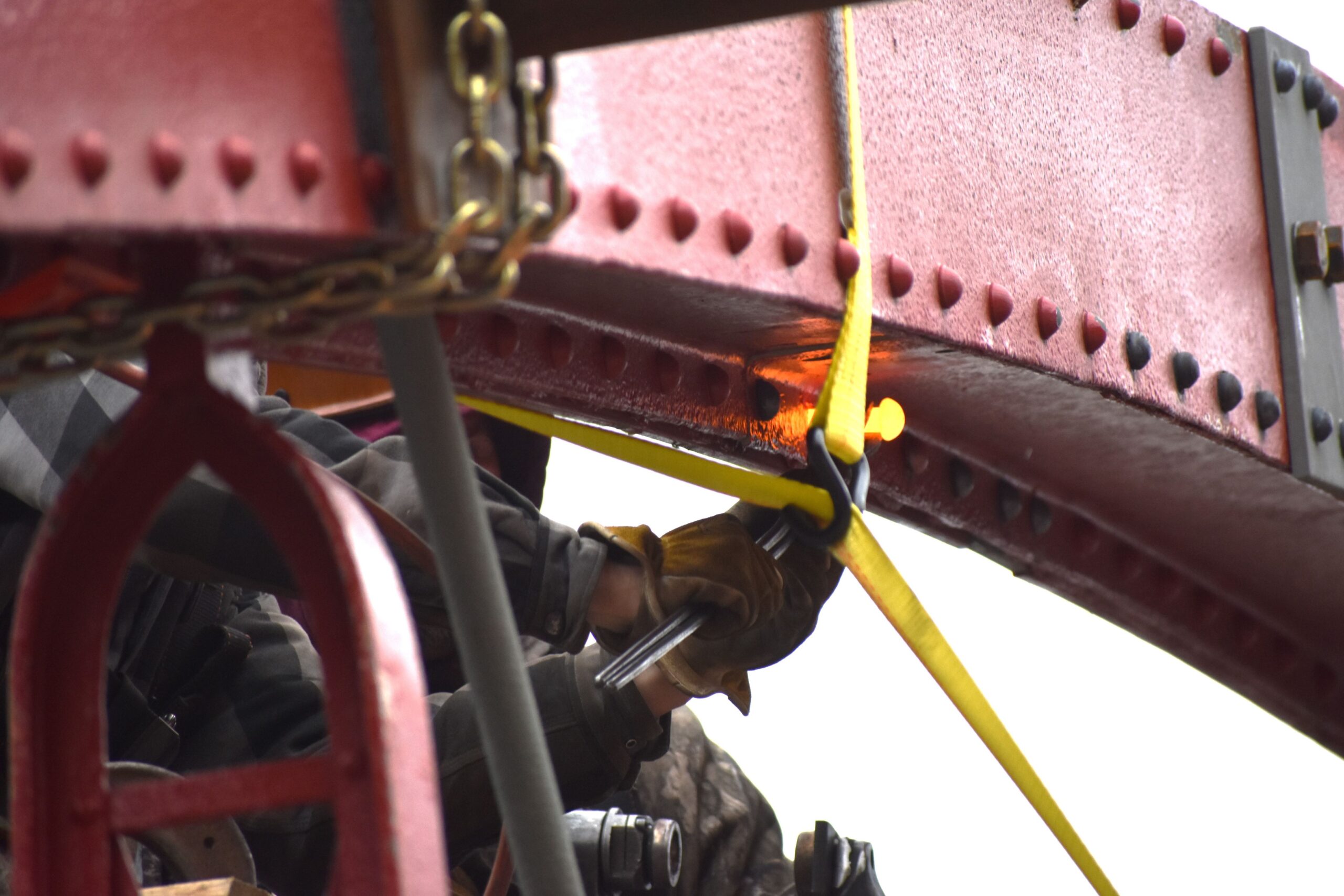 Close up image of a person attaching a strap around a piece of metal.