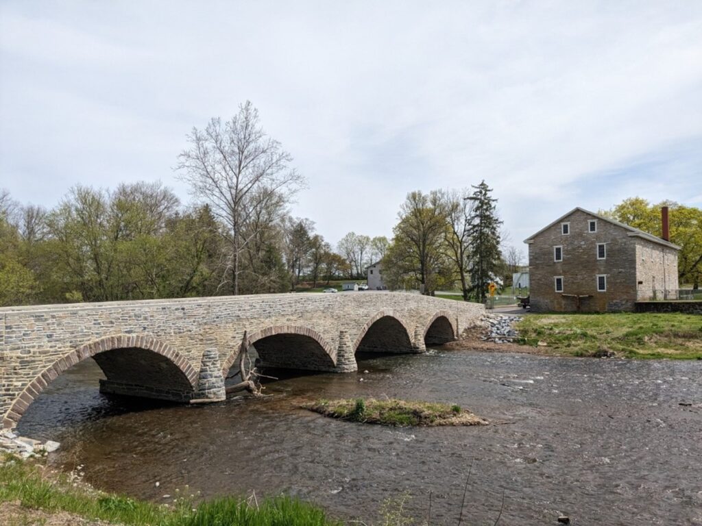 Low stone arched bridge over water and next to a stone building.