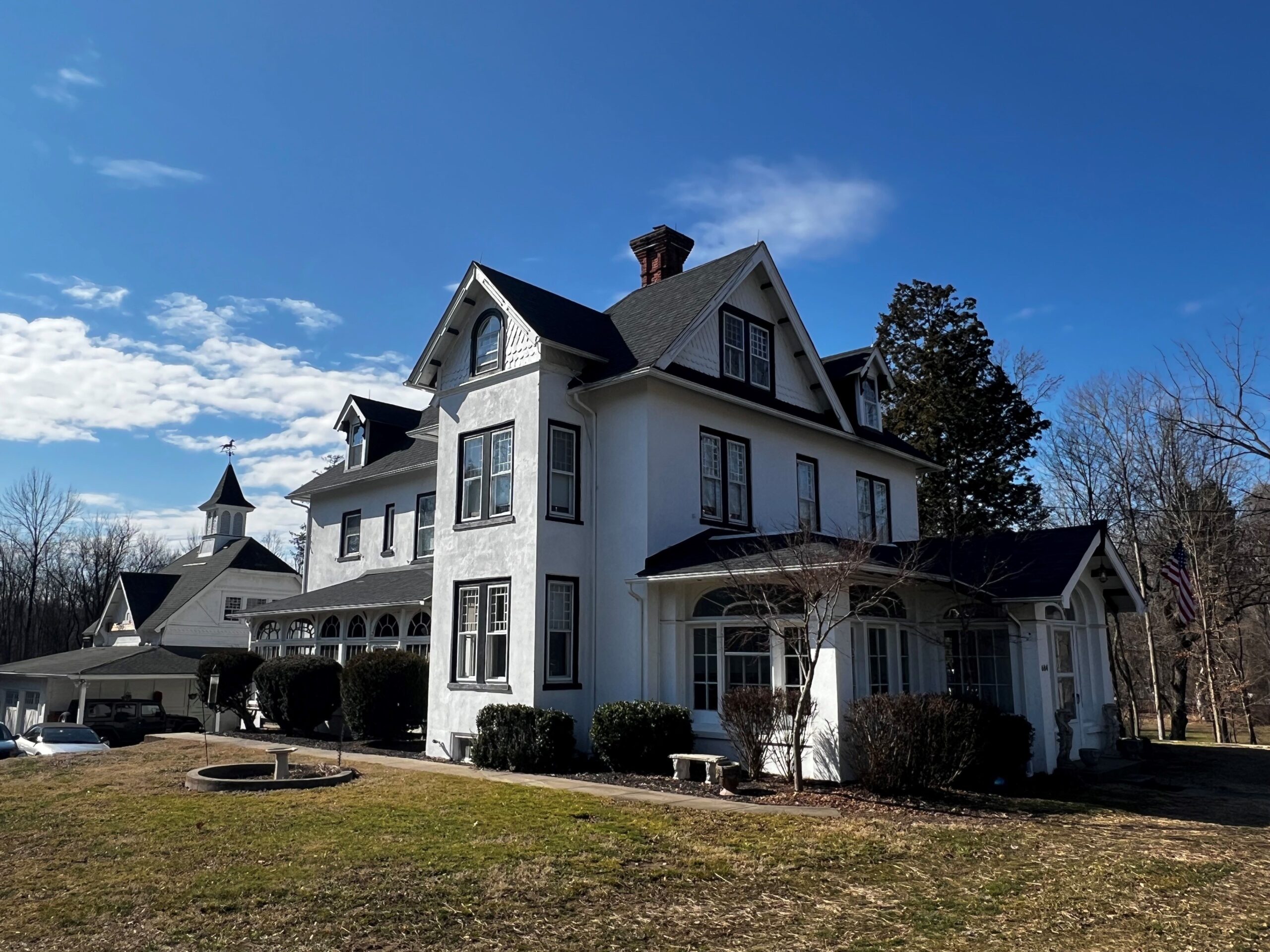 Two story white stucco house with many windows and porches surrounded by lawns.