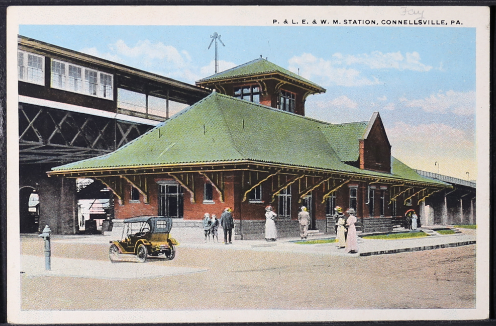 Color postcard of brick building with people and cars.