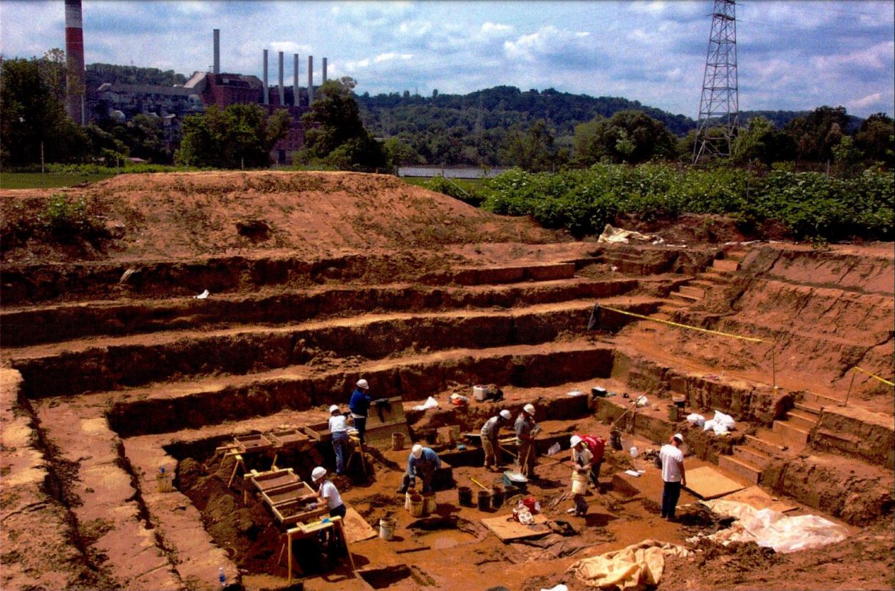 People stand at bottom of very large square hole cut into the earth.