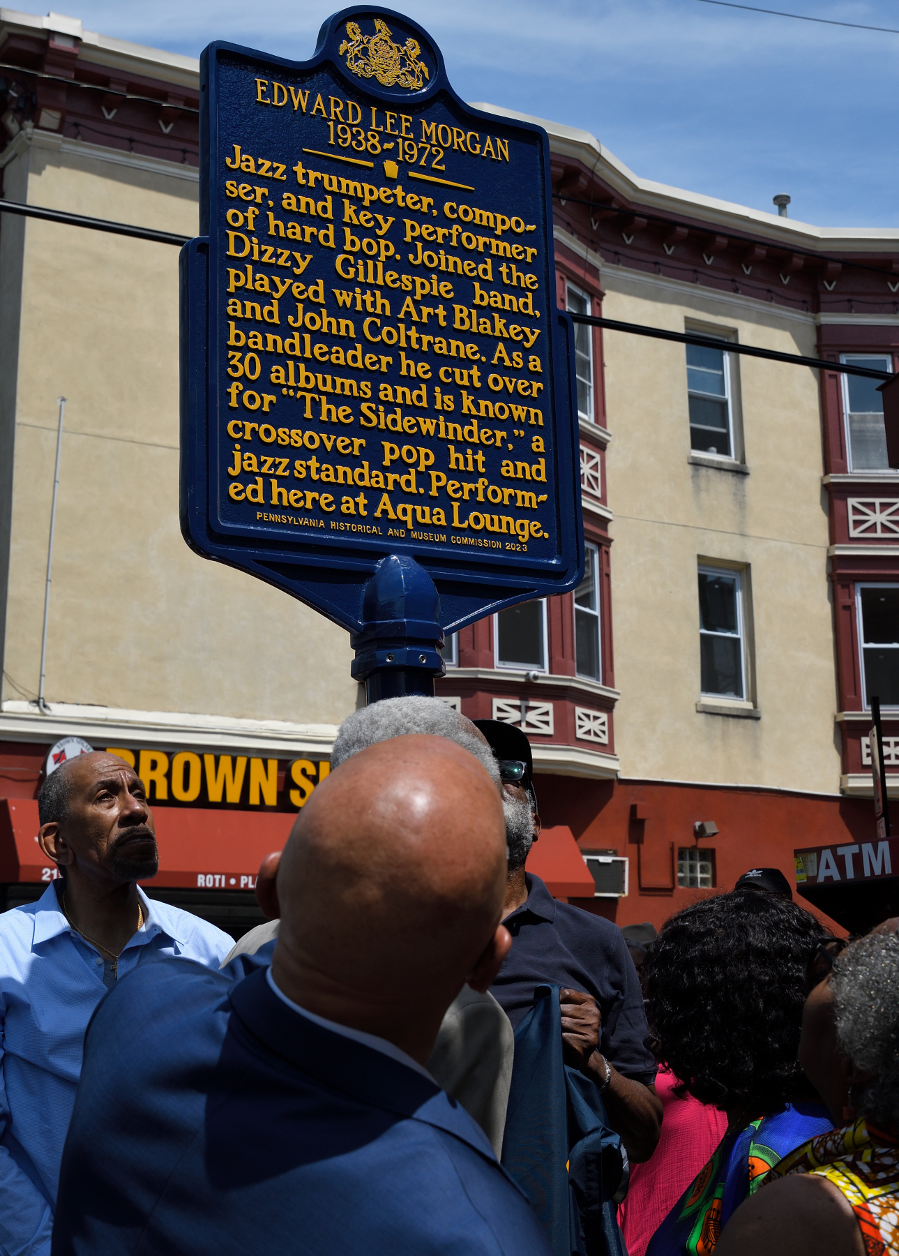 People looking up at tall metal sign on a city block.