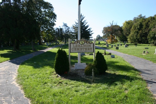 Sign in front of flagpole on small grassy area with paved paths on either side.