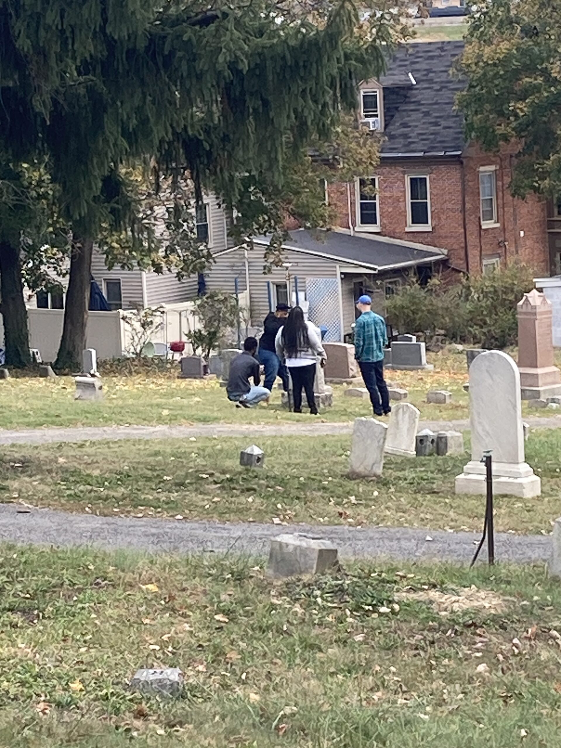 Group of people stand in front of grave marker in grassy area.