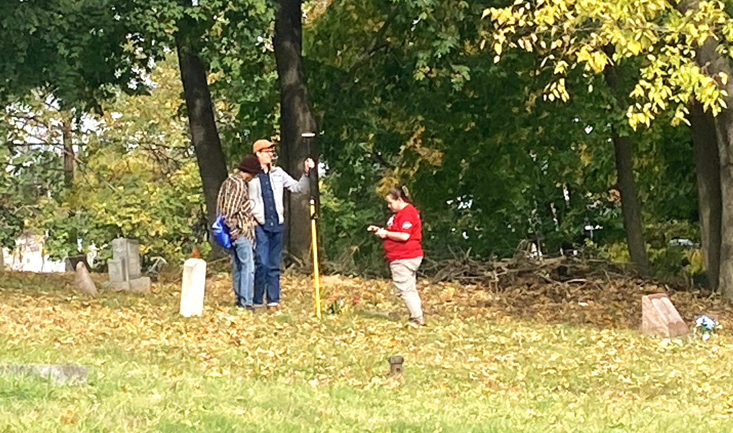 Three people standing in grassy area with tress in background.