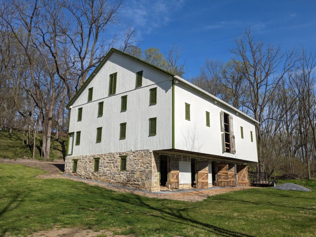 Large wood and stone barn surrounded by trees and grass.