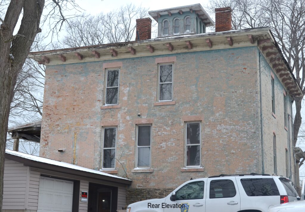 Two story brick building with small one-story garage and car at back.