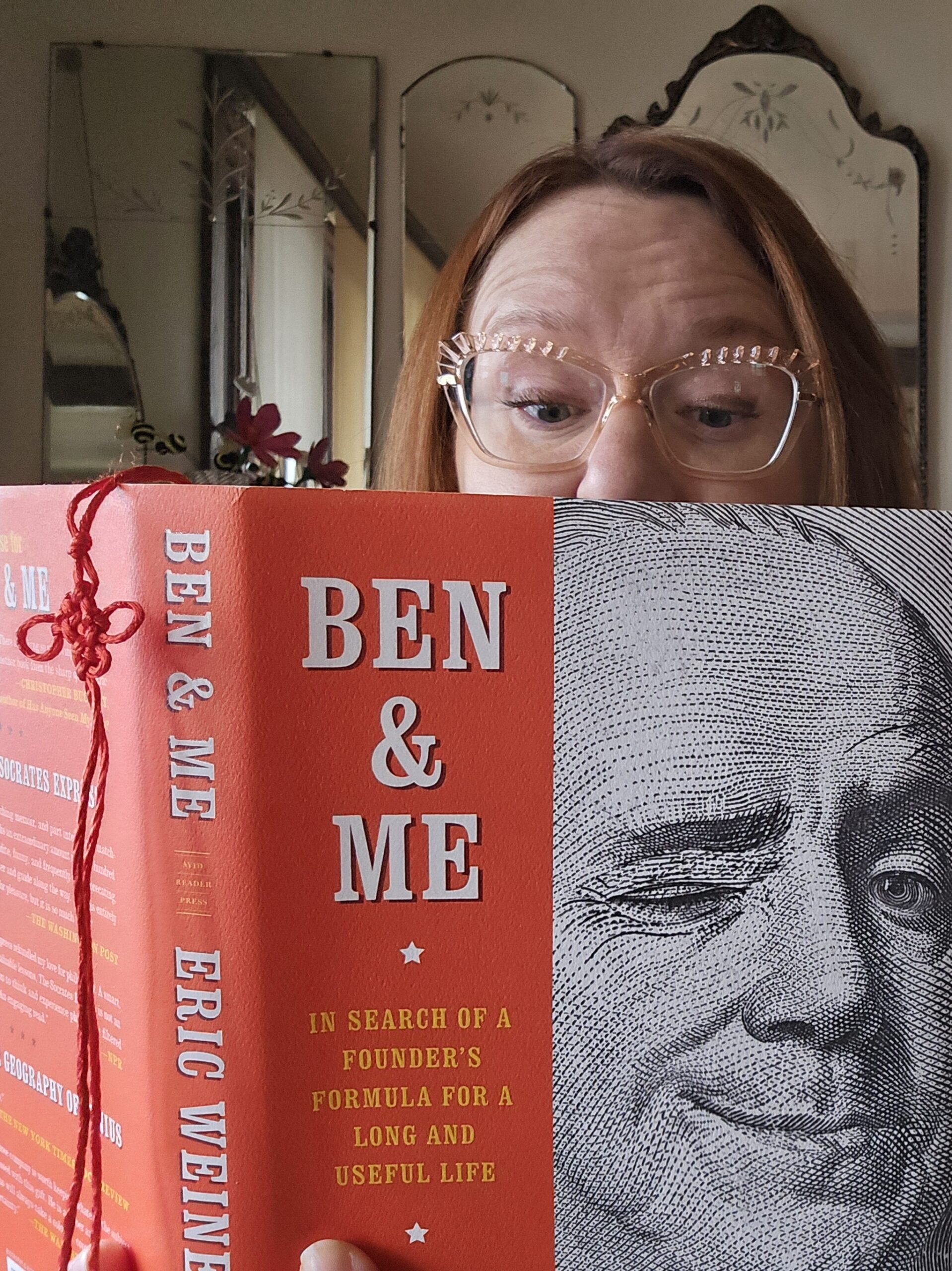 Woman wearing glasses with a book in front of her lower face.