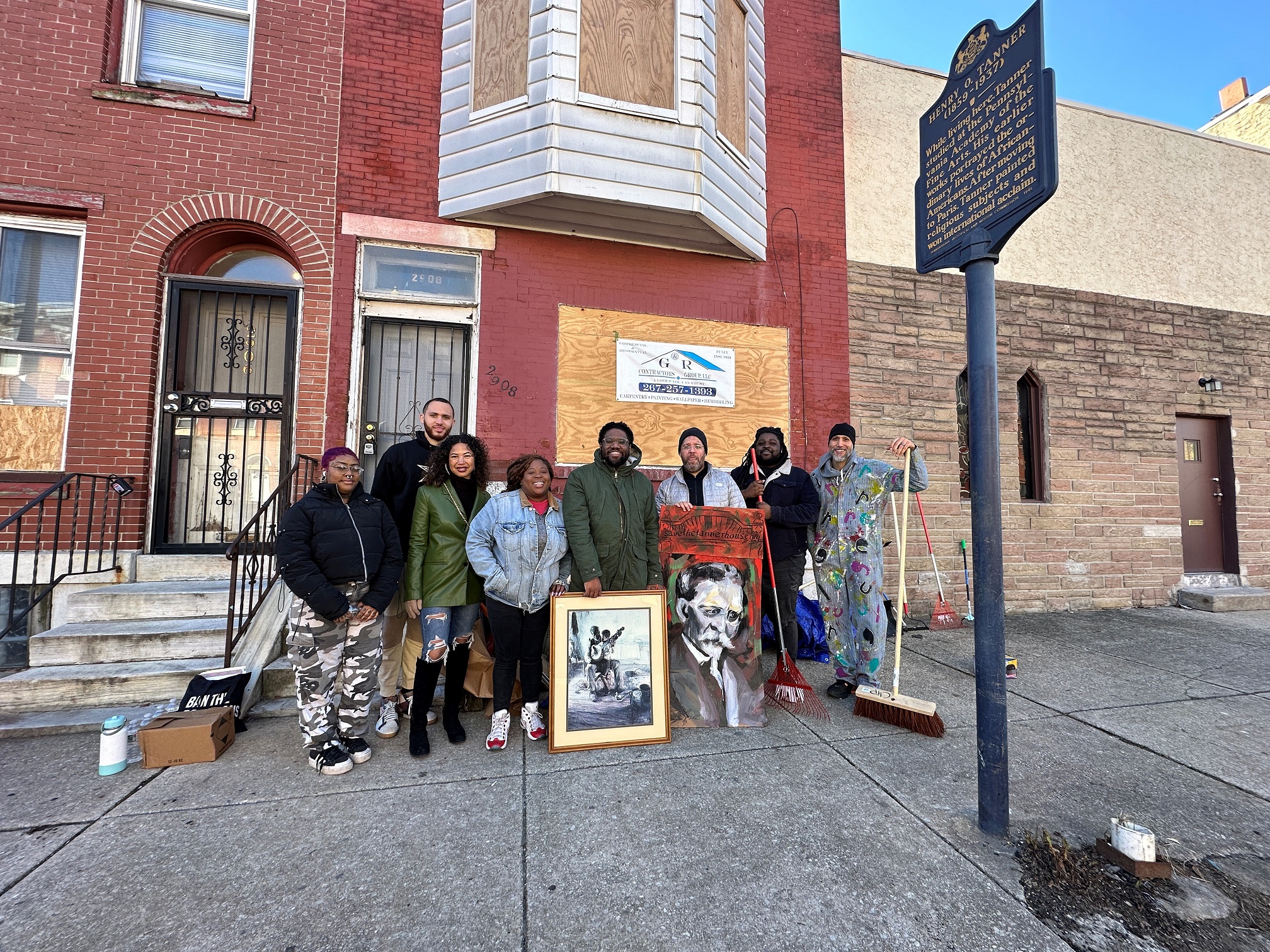 Group of people stand on a sidewalk in front of a brick building.