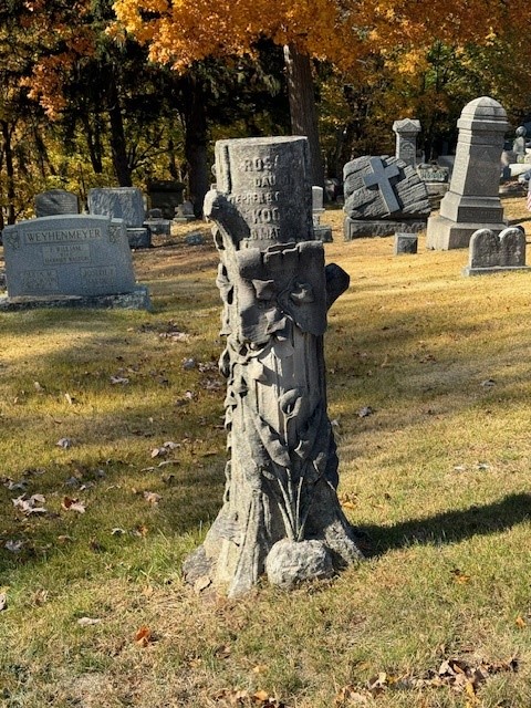 Tall masonry grave marker fashioned to look like a tree stump with flowers.