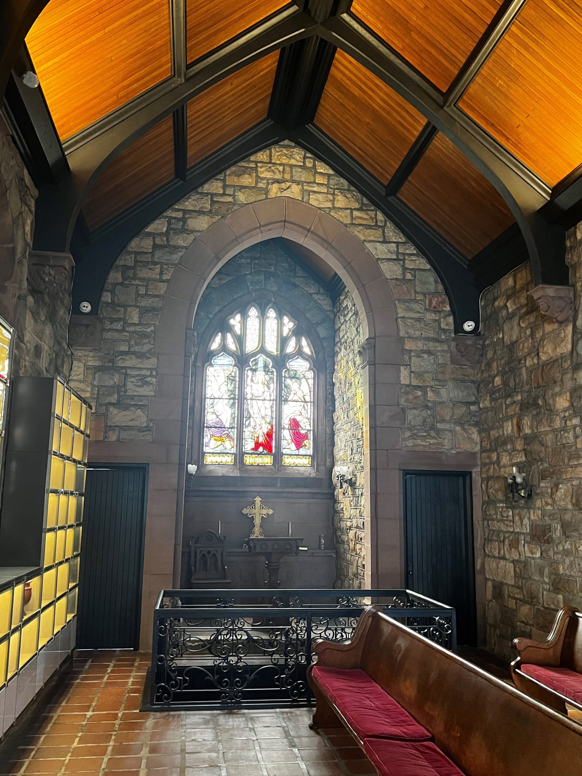 Inside a small building with tile floors, stone walls, benches, stained glass, and a high ceiling.