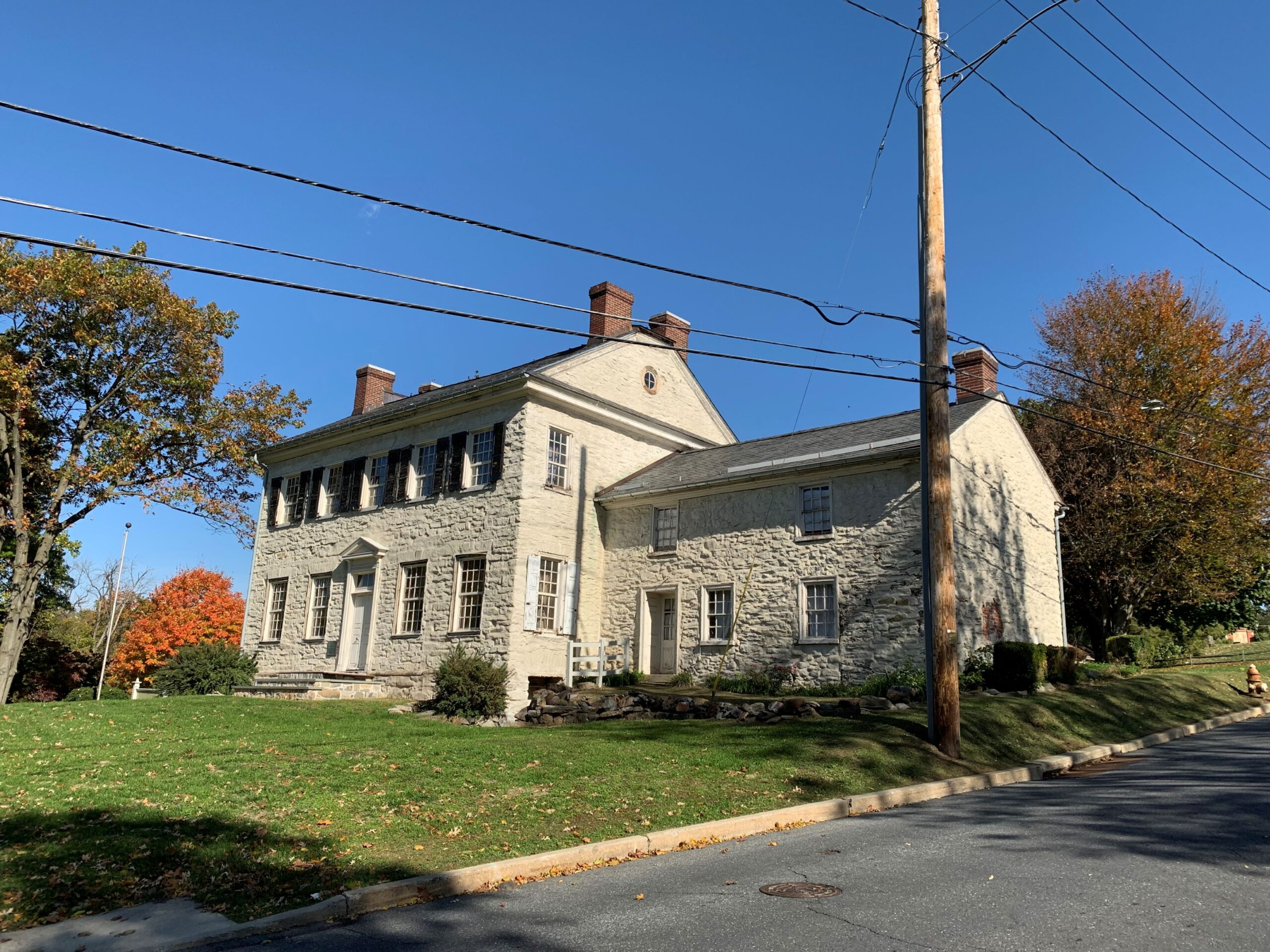 Two-story stone house with stone addition surrounded by grass and next to a paved surface.