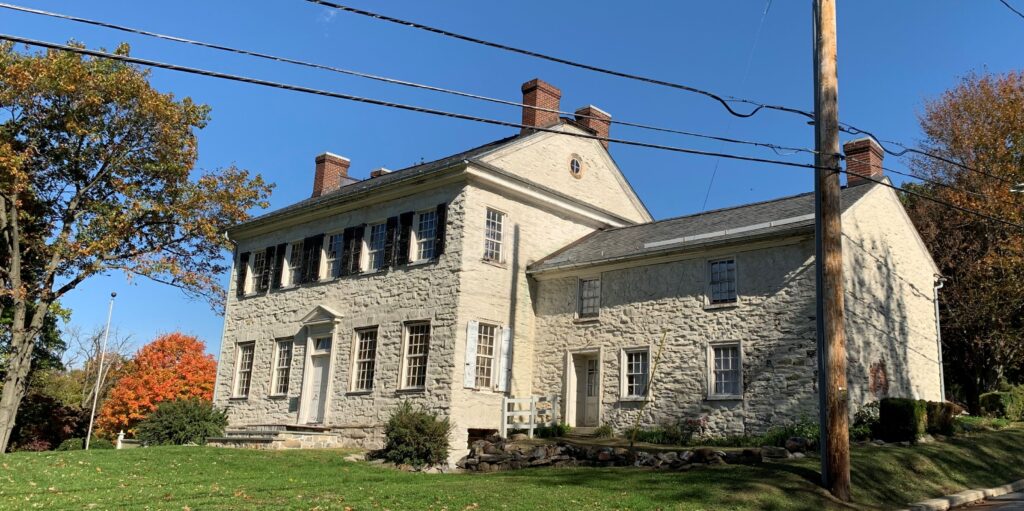 Two-story stone house with stone addition surrounded by grass.