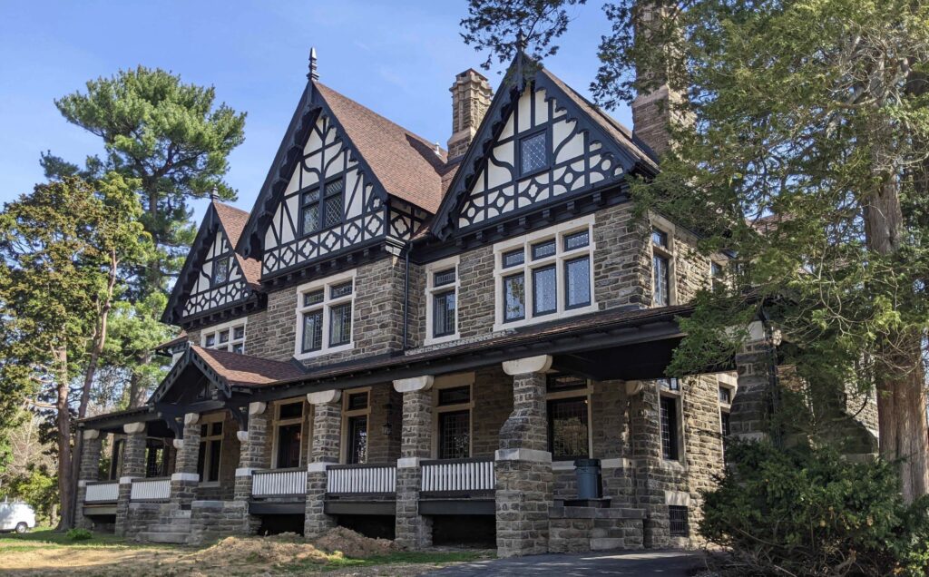 Large three story stone house with deep front porch and three gables on the roof.