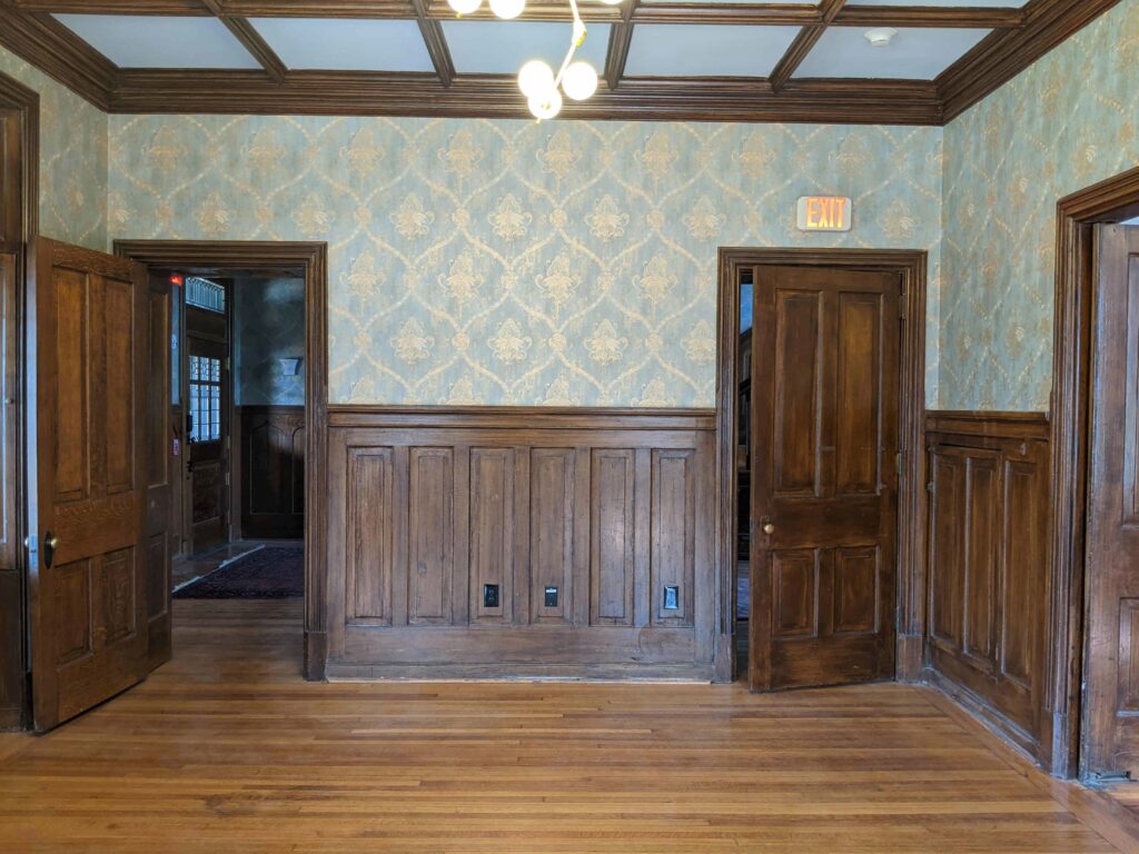 Room with two doors at one end and walls with wood panels and wallpaper.