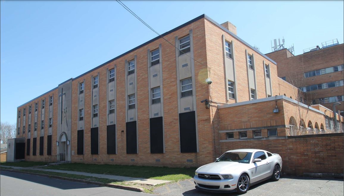 Three story brick building with center entrance, vertical window bays, and flat roof.