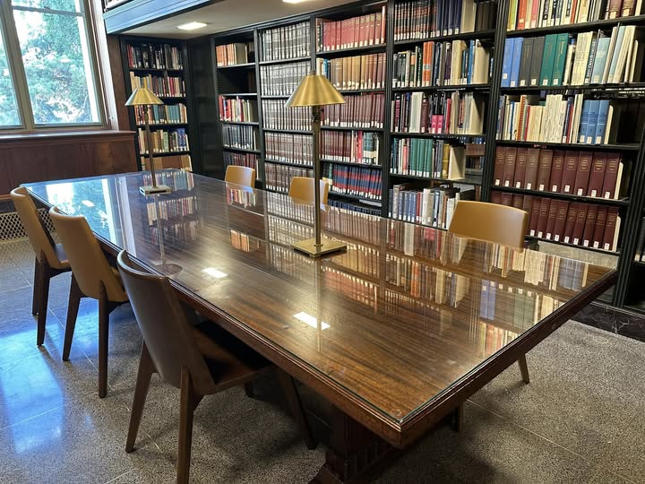 Room with large wood table, book shelves lining the walls and large window.